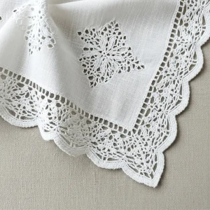 Detalle de blonda de algodón blanca con patrón floral, mostrando su textura natural y suavidad. Ideal para ropa de bebé y lencería confortable.