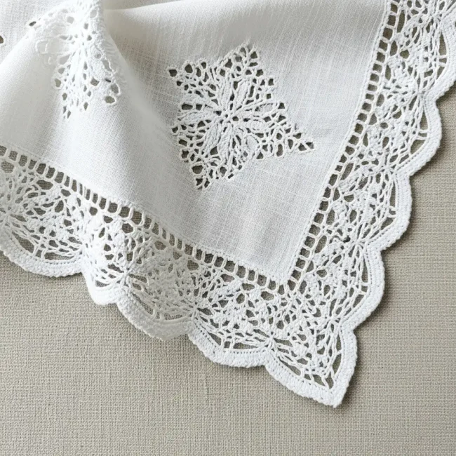 Detalle de blonda de algodón blanca con patrón floral, mostrando su textura natural y suavidad. Ideal para ropa de bebé y lencería confortable.