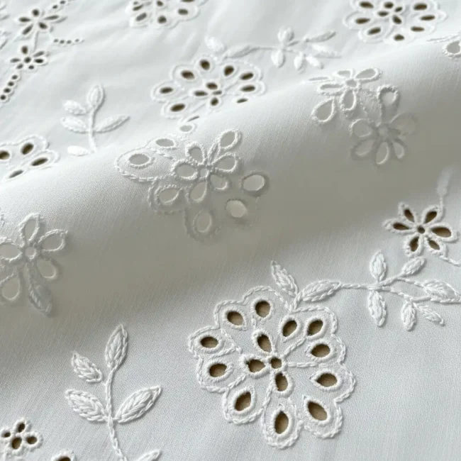 Detalle de Bordado Inglés sobre tela de batista de algodón blanca, con calados florales y puntadas de ojal. Técnica de bordado whitework.