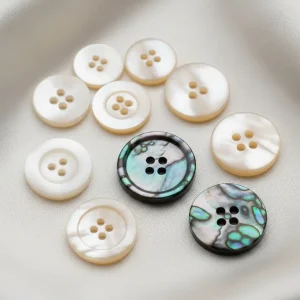 Colección de botones de nácar (madreperla) de diferentes tipos (Akoya, Trochus, Tahití) sobre tela de seda, mostrando su brillo iridiscente. Botones de lujo.