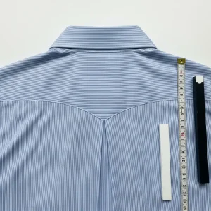 Detalle del canesú trasero doble de una camisa de algodón azul claro, mostrando su costura y el pliegue de la espalda. Pieza clave en patronaje.