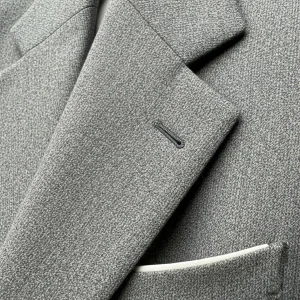 Detalle de un cuello vuelto con solapa de muesca en un blazer de lana gris. Técnica de sastrería para chaquetas y abrigos formales.