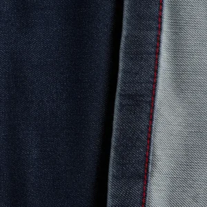 Macro de tejido denim selvedge crudo, mostrando su textura de sarga diagonal, color índigo y orillo con línea roja. Tela de algodón resistente para jeans.