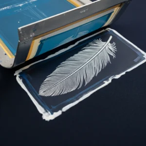 Estampación por descarga de color sobre tela de algodón azul, mostrando un patrón de plumas creado al eliminar el tinte. Técnica de impresión textil.