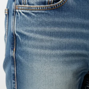 Detalle de unos jeans de denim deslavado mostrando el efecto de desgaste y los "bigotes". Proceso de acabado para ropa casual.