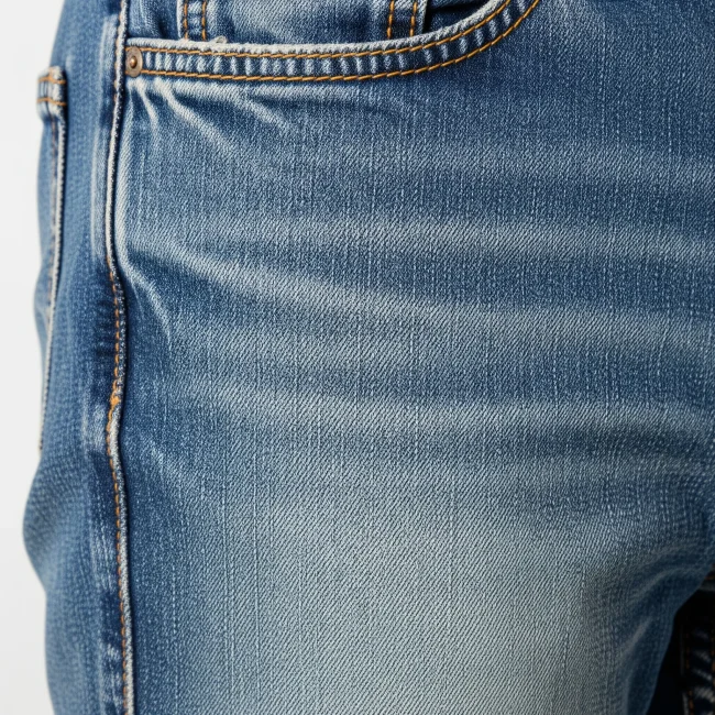 Detalle de unos jeans de denim deslavado mostrando el efecto de desgaste y los "bigotes". Proceso de acabado para ropa casual.