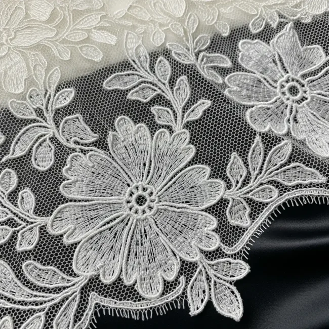 Macro de encaje cordoné tipo Alençon color marfil, mostrando sus motivos florales delineados con un cordón en relieve sobre tul. Encaje de lujo para novias.