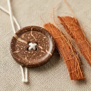Botón de coco pulido y fibras de coco crudas (bonote) sobre tela de lino. Fibra natural resistente para esteras, cepillos y botones.