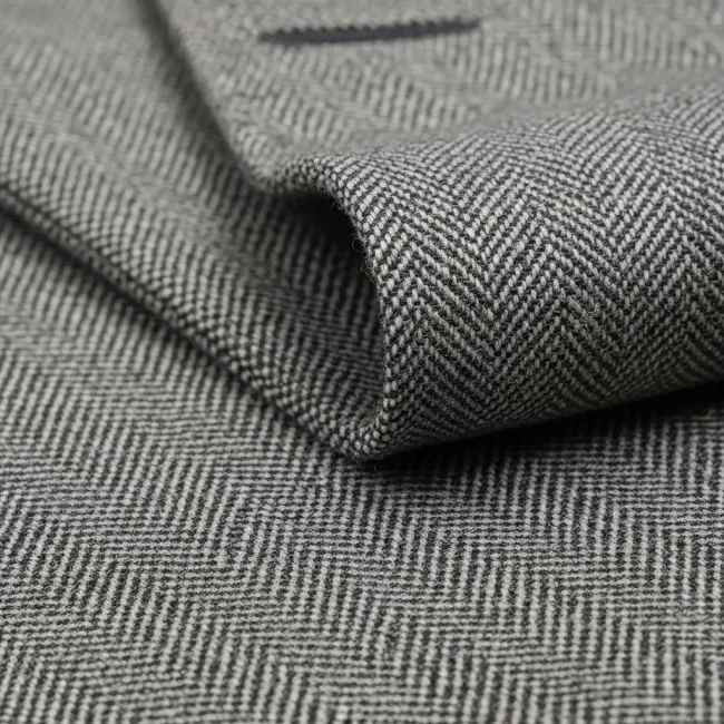 Macro de tejido Cheviot de lana con patrón de espiga en tonos grises. Tela resistente y duradera para trajes y abrigos.